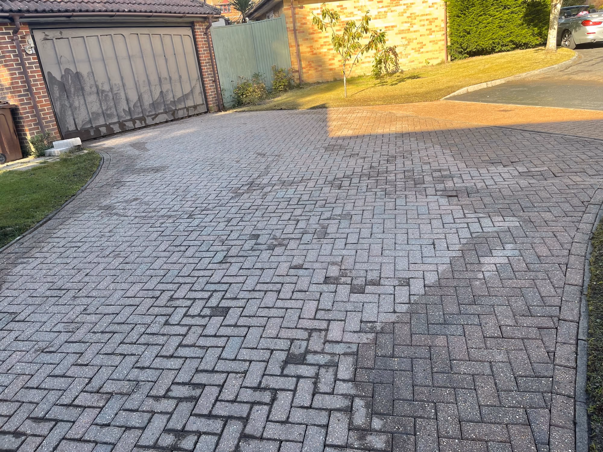 A block paved driveway beside a garage, half of it still in shade and darkened with algae, the other half catching low sun