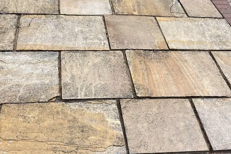 The same run of sandstone flags after cleaning, each slab a different shade of buff and rust, with the brick edging clear